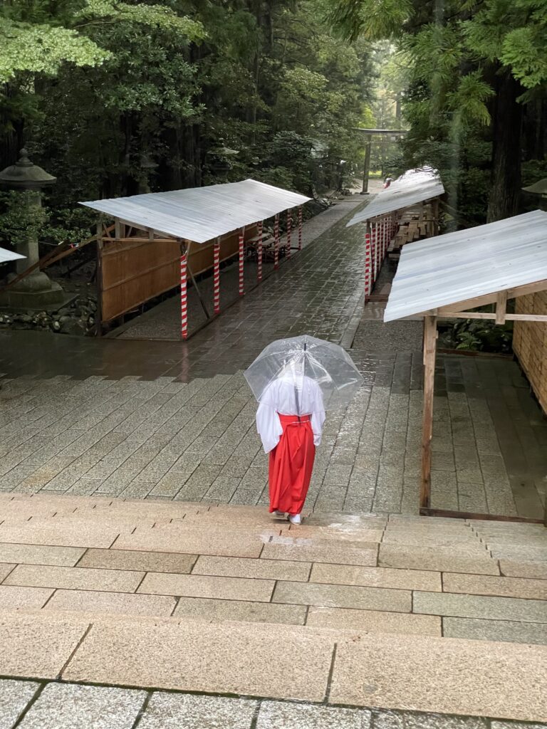 雨の彌彦神社境内を歩く巫女